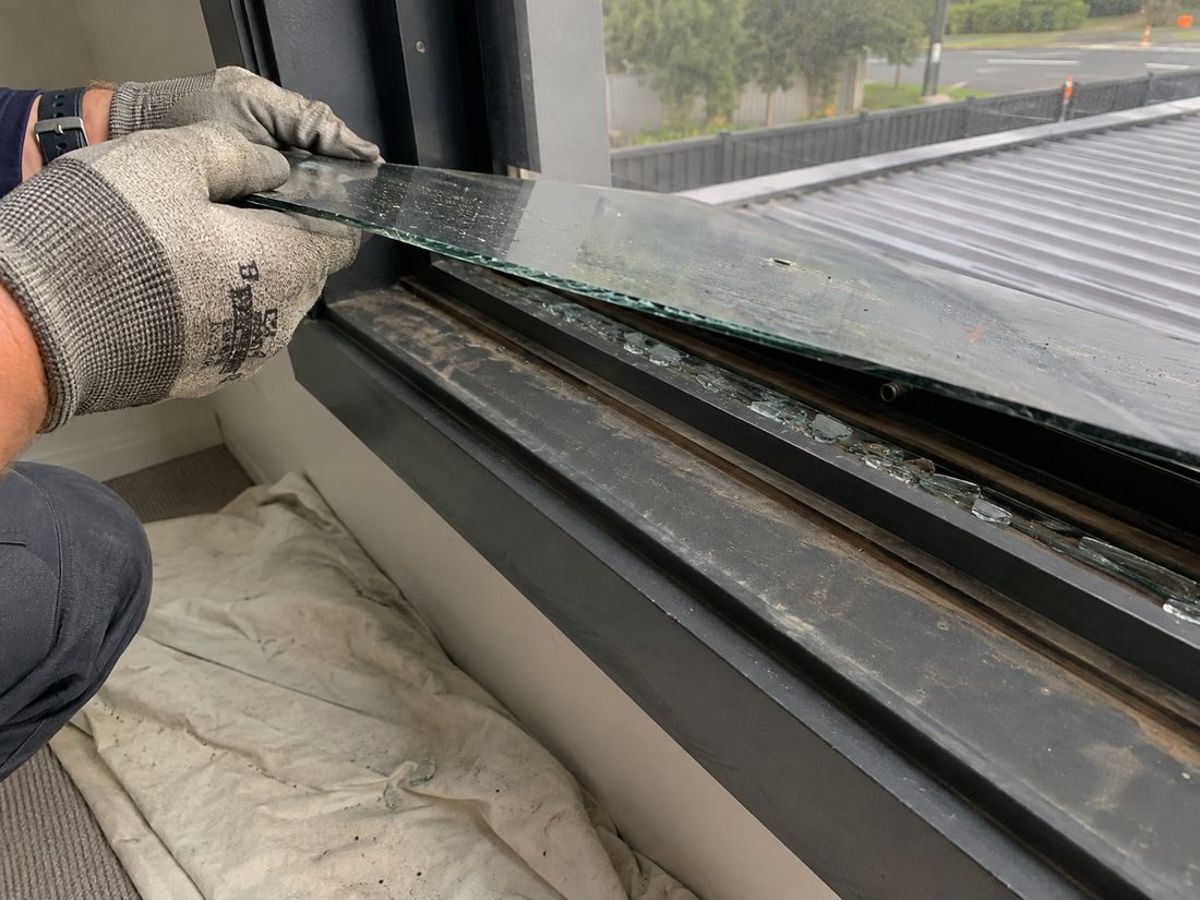 Glazier in cut resistant gloves lifting a cracked pane out of a dark aluminium window frame